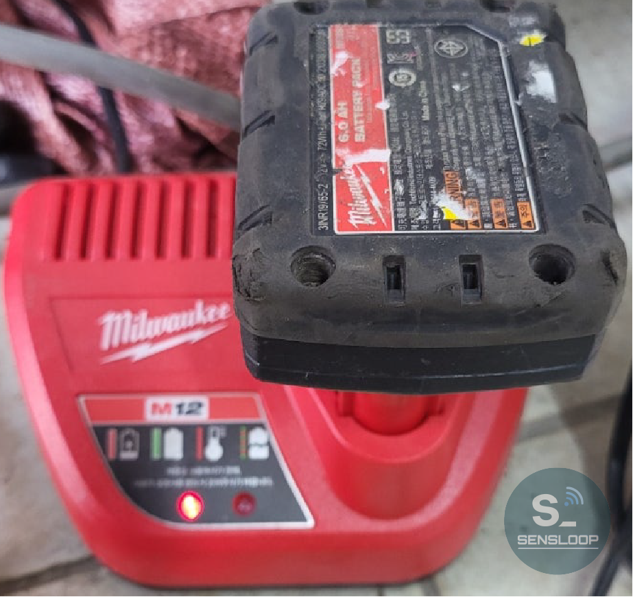 수리된 밀워키 M12 6.0Ah 배터리를 정품 충전기에 연결하여 정상 충전 여부를 테스트하는 모습.